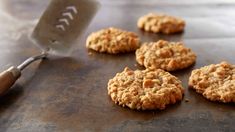 some cookies are on a baking sheet with a cookie spatula next to it and six oatmeal cookies in the foreground