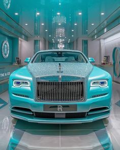 the front of a blue rolls royce parked in a showroom with chandeliers hanging from the ceiling