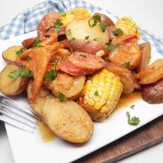 a white plate topped with potatoes and corn on the cob next to a fork