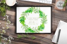 a watercolor wreath with the words jesus surrounded by greenery on a wooden table