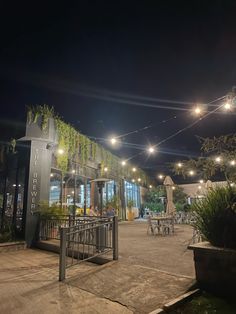 an outdoor area with tables, chairs and lights on the side of it at night