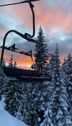 a ski lift going up the side of a snowy mountain at sunset with trees in the foreground