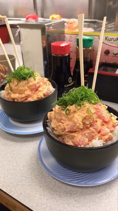 two black bowls filled with food on top of a counter next to chopsticks