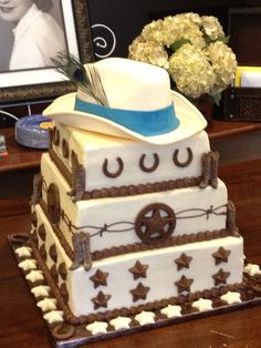 a cake with a cowboy hat on top is sitting on a table in front of a framed photo