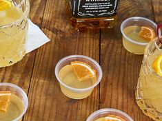 several glasses filled with lemonade and orange slices on top of a wooden table next to a bottle of whiskey