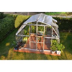 a small greenhouse in the middle of a yard with potted plants and other items