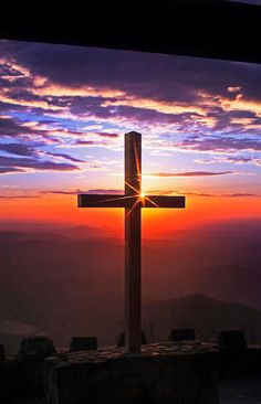 a cross on top of a hill with the sun setting in the distance behind it