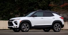 a white suv is parked in front of a concrete wall and some trees on the other side