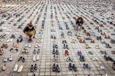 two people kneeling on the ground surrounded by hundreds of shoes