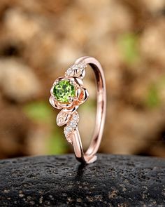 a rose shaped ring with green and white stones on it's sides, sitting on top of a rock