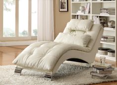 a white chaise lounge chair sitting in front of a book shelf filled with books