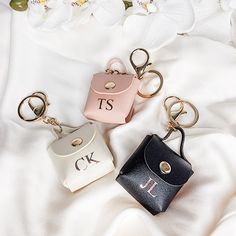 three keychains with initials on them sitting on a white blanket next to flowers