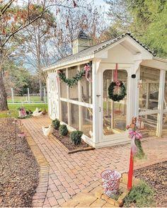 a small white chicken coop with wreaths on the door and windows in front of it