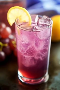 a close up of a drink on a table with grapes and lemons in the background