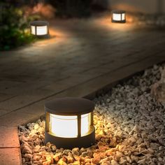 some lights that are on the ground in the grass and rocks near a path with stones