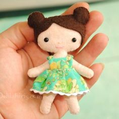 a hand holding a tiny doll in a green dress