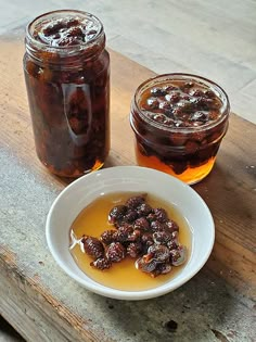 two jars filled with honey and raisins on top of a wooden table next to a white bowl