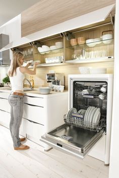 a woman standing in front of an open dishwasher with dishes on the shelves