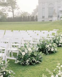 rows of white folding chairs lined up in front of a building with flowers on the grass