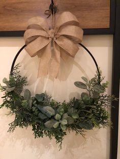 a wreath hanging on the wall next to a wooden sign with a bow and greenery