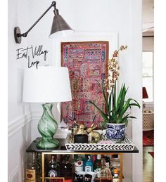 a table with vases and plants on it in front of a wall hanging tapestry