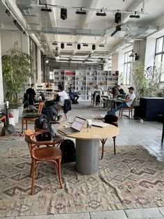 people are sitting at tables in an open area with many bookshelves and plants