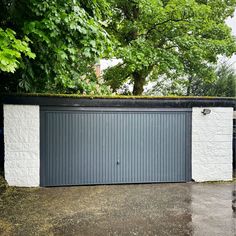 an open garage door on the side of a white brick building with trees in the background