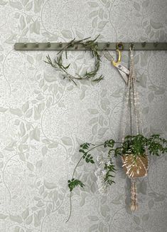 two plants hanging from hooks on a wall with a floral pattern in the back ground