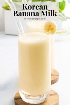 two glasses filled with banana milk sitting on top of a wooden coaster next to a plant