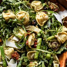 a wooden bowl filled with pasta and veggies on top of a white table