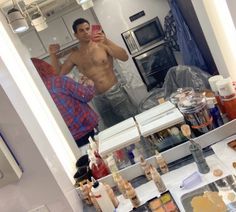 a shirtless man taking a selfie in front of a mirror with food on the counter