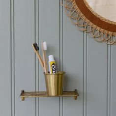 two toothbrushes are sitting in a cup on a shelf next to a mirror