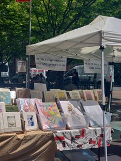 there are many paintings on display under the umbrellas at this outdoor art market,