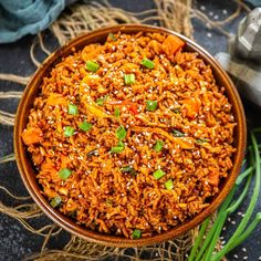 a bowl filled with rice and carrots on top of a table next to green onions