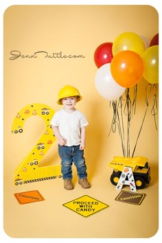 a young boy standing in front of a number two sign with balloons and construction equipment