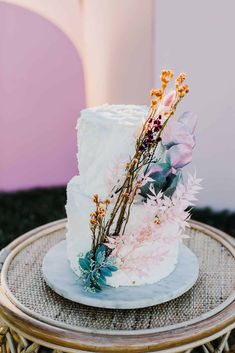 a white wedding cake with flowers on top sitting on a wicker table in front of a pink wall