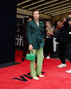 a man in a green suit standing on a red carpet with people taking pictures behind him