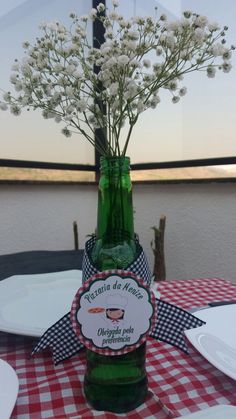 a green bottle with flowers in it sitting on a table next to plates and utensils