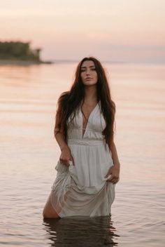 a woman standing in the water with her hands on her hips and wearing a white dress