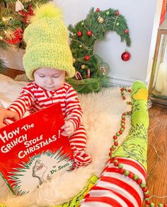 a baby is sitting on the floor reading a book with christmas decorations in the background