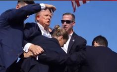 a group of people standing around each other in front of an american flag and two men wearing suits