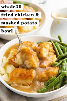 a white bowl filled with chicken and mashed potatoes covered in gravy next to green beans