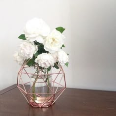 some white flowers are in a glass vase on a wooden table with a light behind it