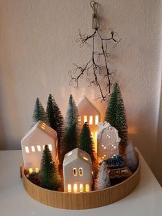 small christmas trees and houses in a wooden bowl with lights on the top, sitting on a table next to a white wall