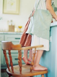 two people standing on top of a wooden chair in a kitchen next to a counter