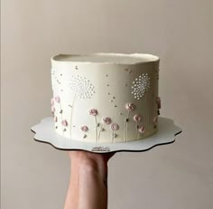 a hand holding a white cake with pink flowers on it