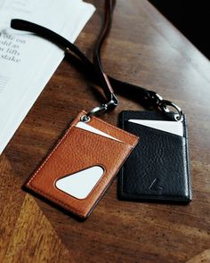 two leather wallets sitting on top of a wooden table next to an envelope and lanyard