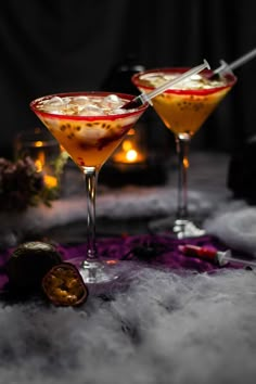 two cocktail glasses with drinks in them on a table