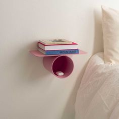 a pink shelf with two books on it next to a white wall and a bed