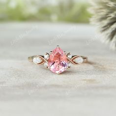 an engagement ring with a pink stone surrounded by white diamonds on a table next to a pine tree